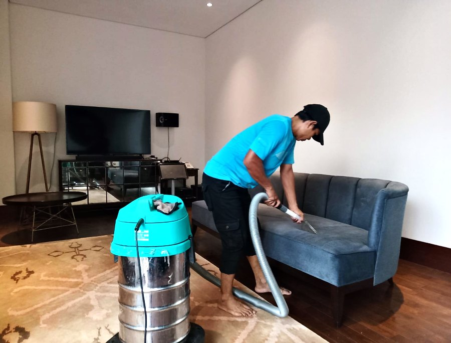 Pekerja memvakum sofa biru di ruang tamu