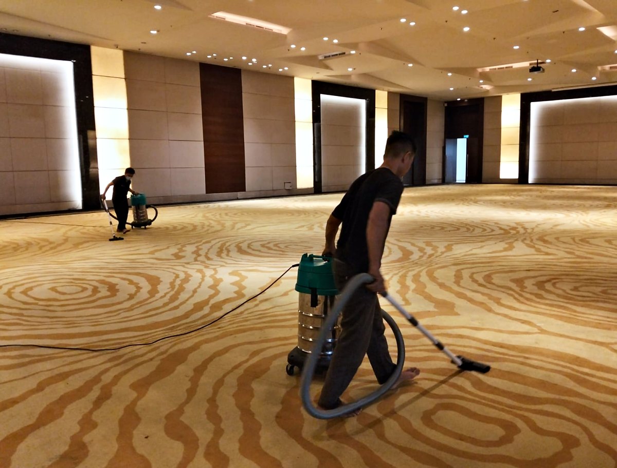 Pekerja IndoCareService memvakum karpet di ballroom