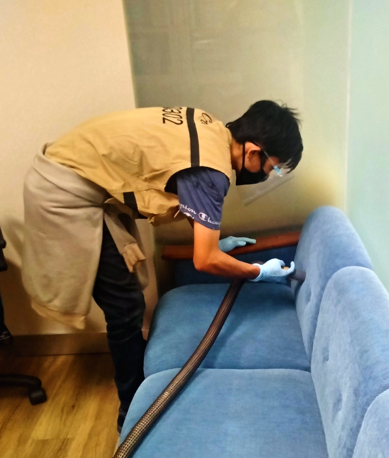 Petugas IndoCareService membersihkan sofa dengan vacuum