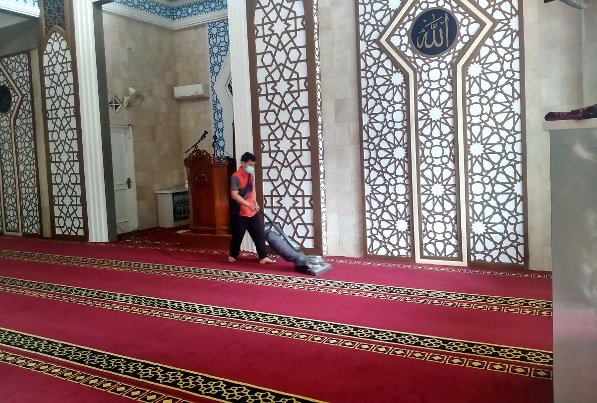 Petugas IndoCareService membersihkan karpet masjid