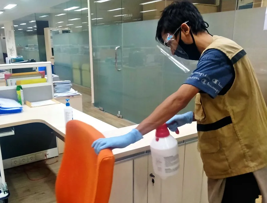 Pekerja menyemprot disinfektan pada kursi kantor